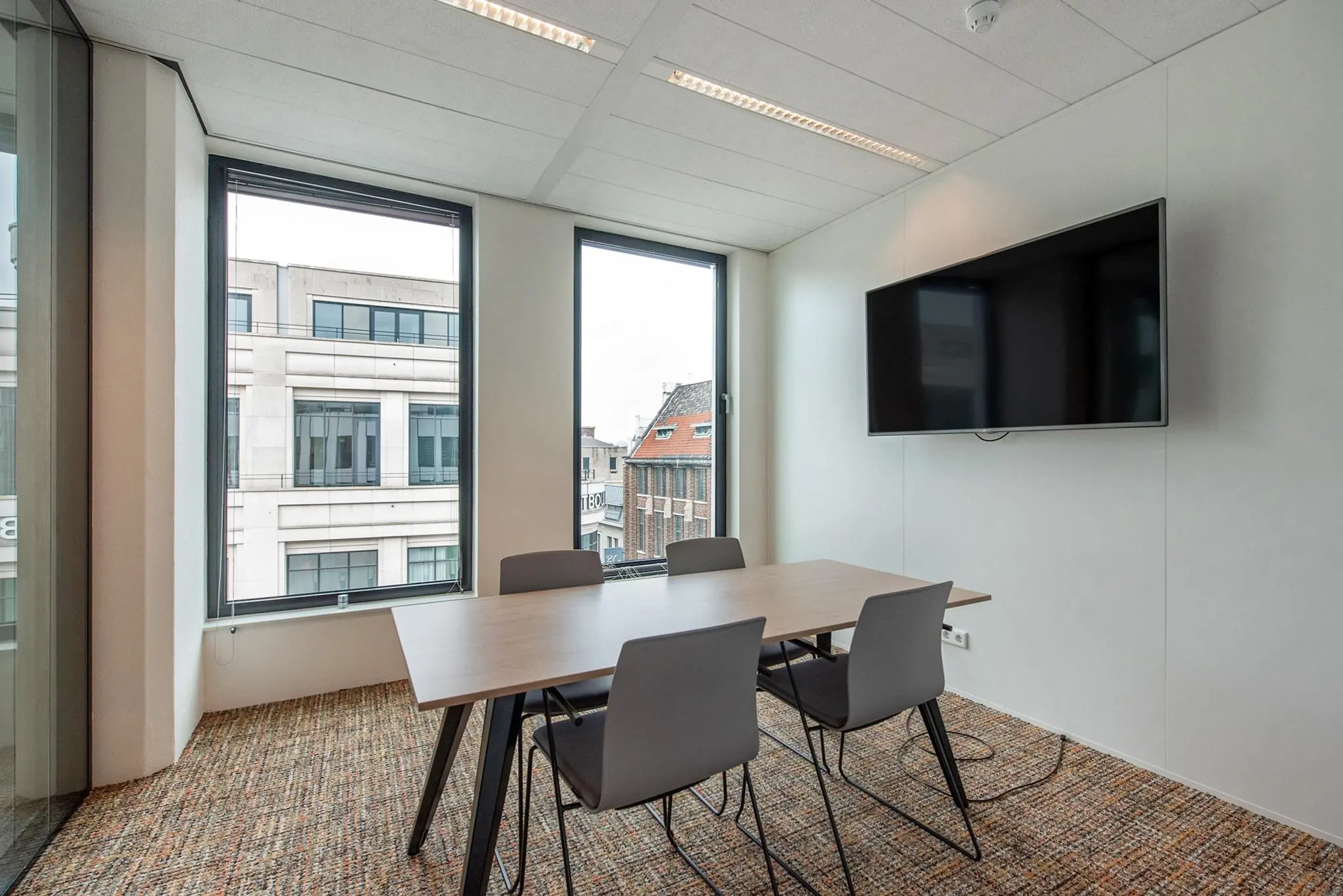 Vergaderruimte met vier stoelen, een tafel, flatscreen en uitzicht op gebouwen aan de Grote Marktstraat.